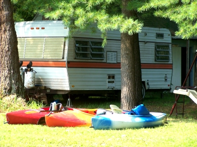 Colorful kayaks resting on the grass beside a camper under the pines